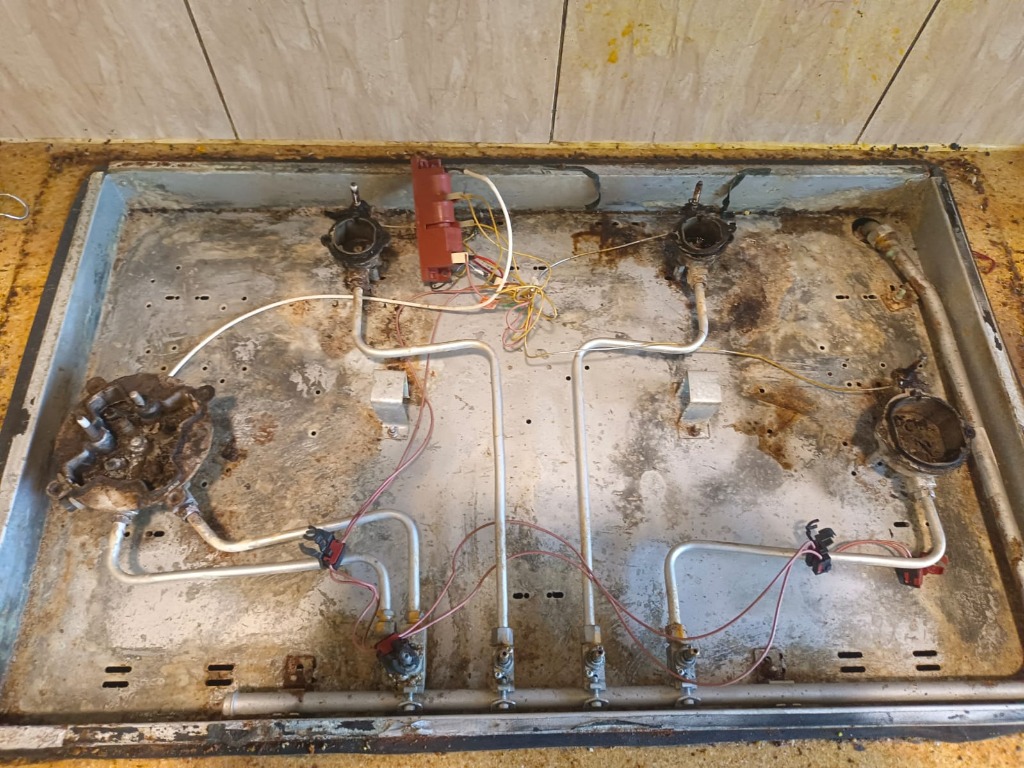 Dirty 4-burner gas stove tray before deep cleaning